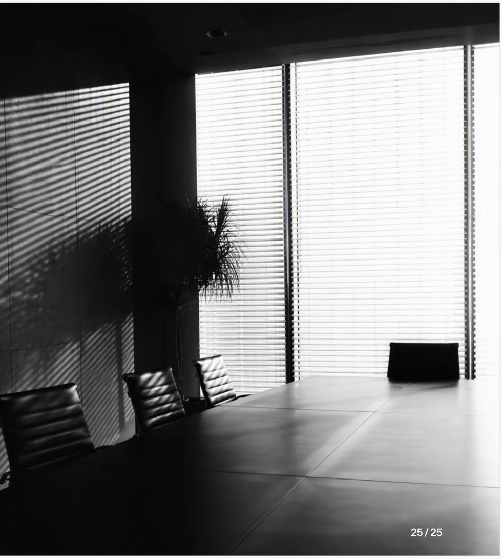 Sala de conselho vazia, em preto e branco, com luz filtrada por persianas